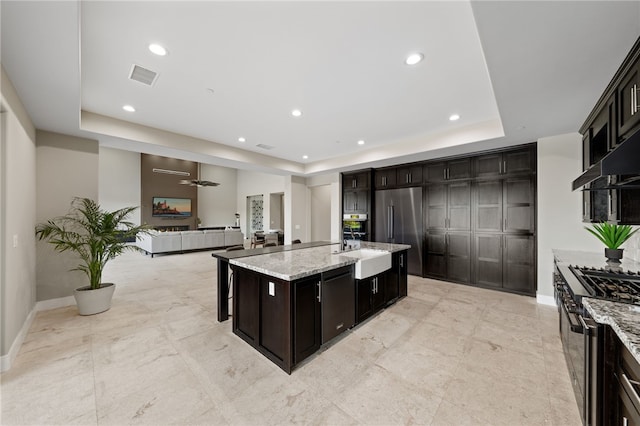 kitchen with a center island with sink, sink, appliances with stainless steel finishes, and a tray ceiling