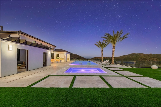 pool at dusk with a mountain view, a yard, an in ground hot tub, and a patio