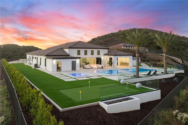 back house at dusk with a fenced in pool, central AC, a mountain view, and a patio