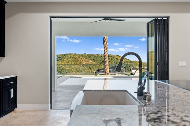 kitchen with light stone counters, sink, ceiling fan, and a healthy amount of sunlight