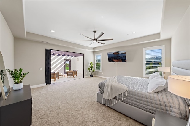 carpeted bedroom with multiple windows, a tray ceiling, and ceiling fan