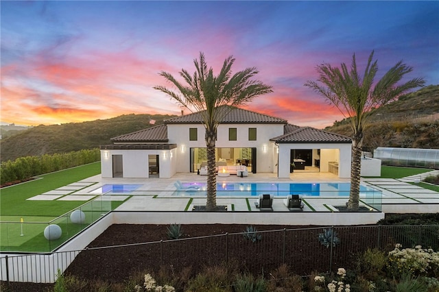 back house at dusk with a mountain view, a patio area, and a fenced in pool