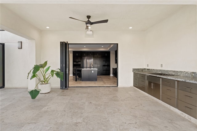 kitchen featuring light stone counters, ceiling fan, and sink