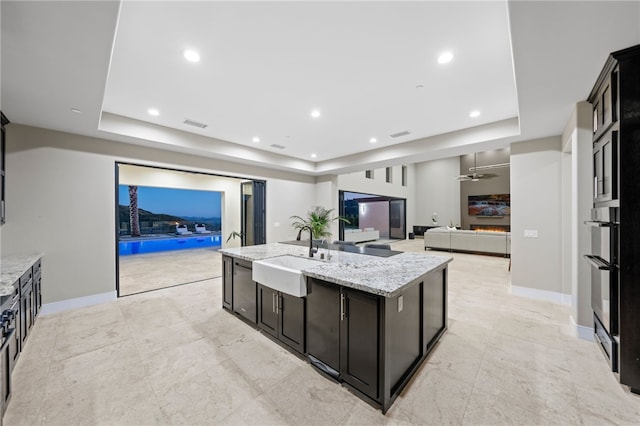 kitchen with light stone countertops, a raised ceiling, ceiling fan, and sink