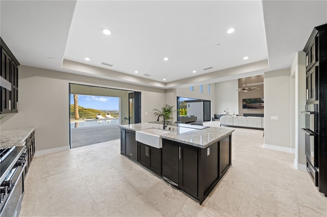 kitchen with sink, a raised ceiling, and an island with sink