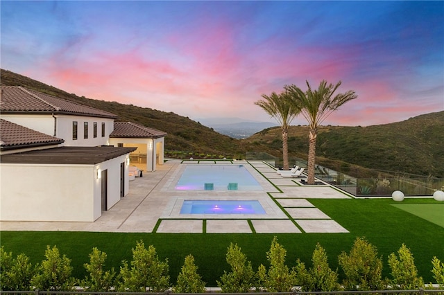 pool at dusk featuring a mountain view, a yard, and a patio