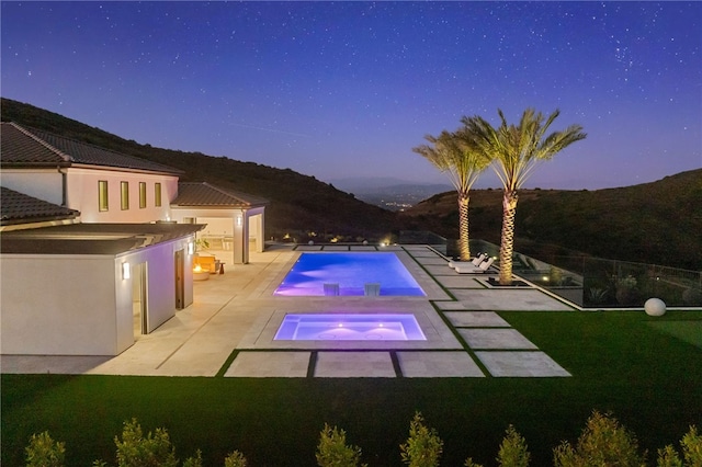 pool at dusk featuring a mountain view, exterior kitchen, a patio, and a yard