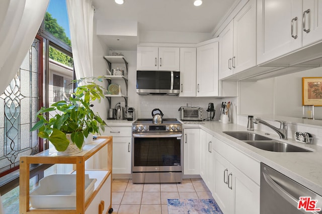 kitchen with appliances with stainless steel finishes, sink, light tile patterned floors, and white cabinets