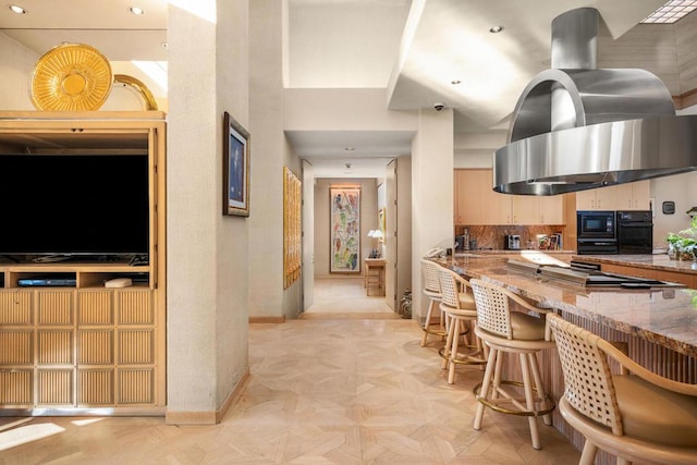 kitchen featuring light parquet floors, island range hood, decorative backsplash, stone counters, and black appliances