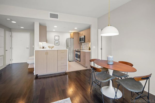 kitchen featuring appliances with stainless steel finishes, dark hardwood / wood-style flooring, tasteful backsplash, light brown cabinetry, and decorative light fixtures