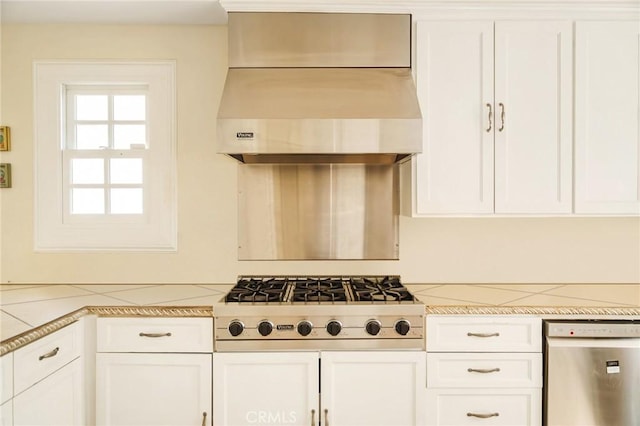 kitchen with light stone countertops, appliances with stainless steel finishes, white cabinetry, and wall chimney exhaust hood