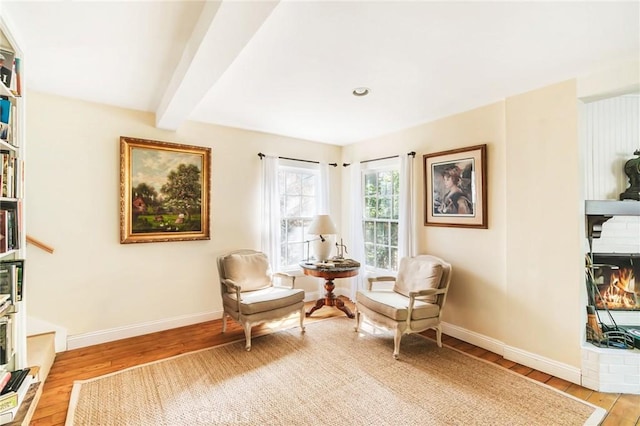 sitting room with beamed ceiling, light hardwood / wood-style flooring, and a brick fireplace