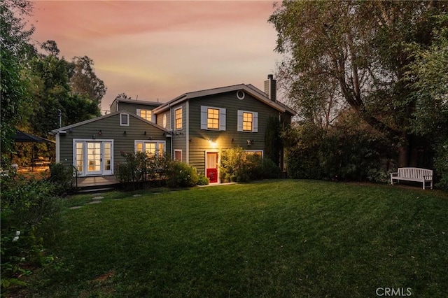 back house at dusk with a lawn and french doors