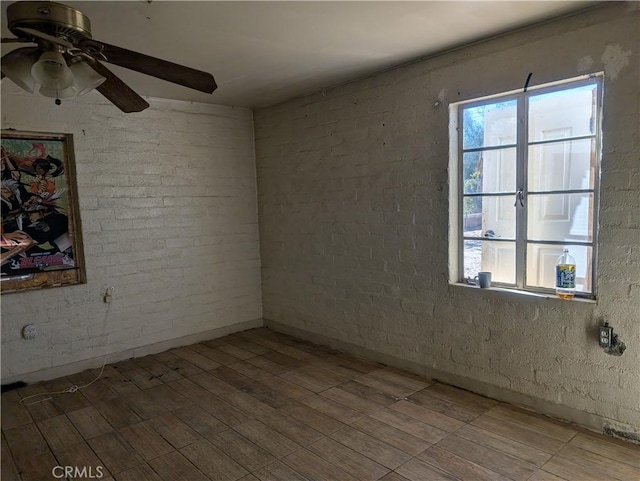 unfurnished room with ceiling fan, brick wall, and hardwood / wood-style floors