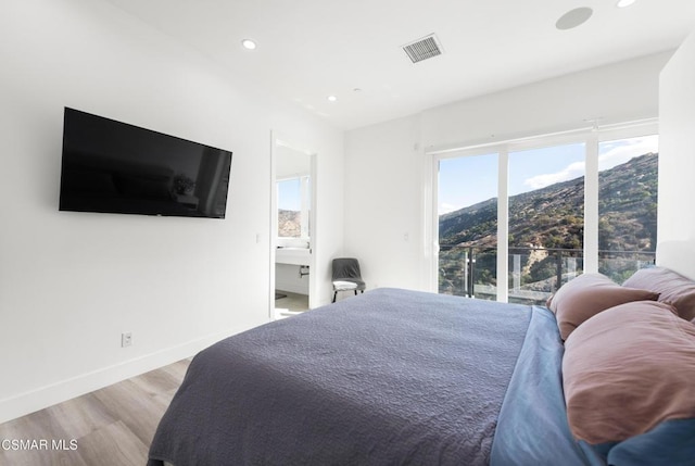 bedroom with a mountain view, light wood-type flooring, and ensuite bath