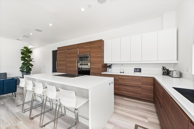 kitchen with a kitchen bar, appliances with stainless steel finishes, light wood-type flooring, white cabinets, and a kitchen island