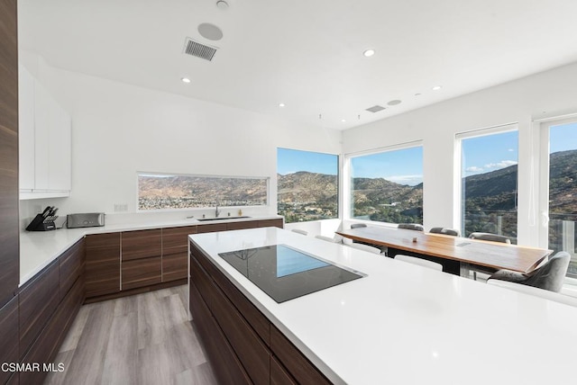 kitchen featuring a mountain view, black electric cooktop, sink, light hardwood / wood-style flooring, and white cabinets