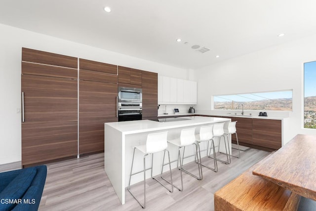 kitchen featuring white cabinets, sink, light hardwood / wood-style flooring, a breakfast bar area, and stainless steel appliances