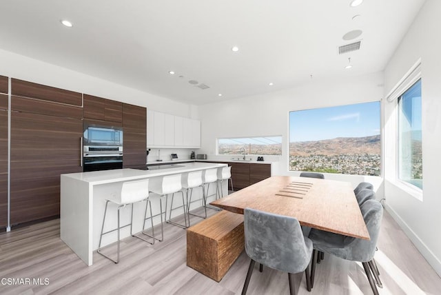 kitchen with white cabinetry, stainless steel appliances, a kitchen bar, a kitchen island, and light wood-type flooring