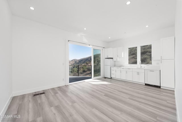 unfurnished living room with a mountain view, sink, and light wood-type flooring