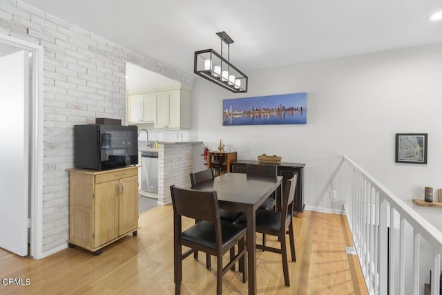 dining space with light wood-type flooring, brick wall, and a chandelier