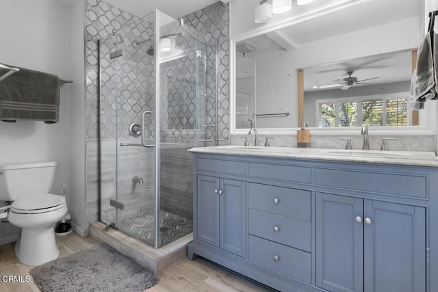 bathroom featuring toilet, wood finished floors, a sink, double vanity, and a stall shower