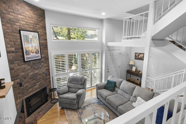 living area featuring a towering ceiling, wood finished floors, stairs, a brick fireplace, and recessed lighting