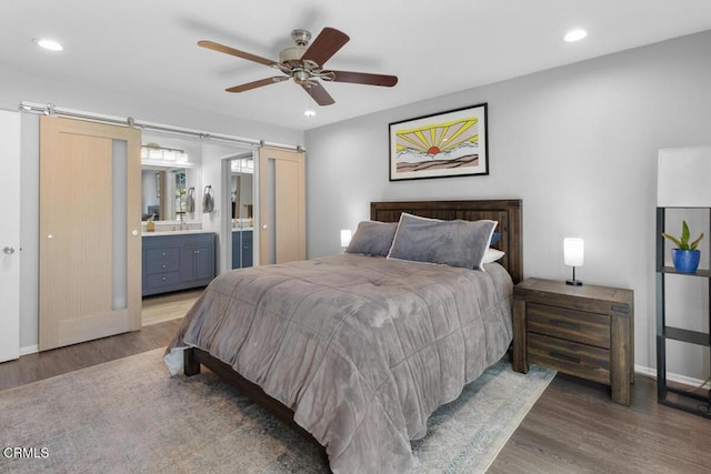 bedroom with a barn door, recessed lighting, wood finished floors, a ceiling fan, and ensuite bath