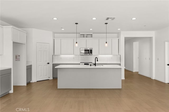 kitchen with a kitchen island with sink, stainless steel microwave, visible vents, and light wood-type flooring