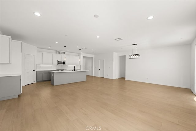 unfurnished living room featuring recessed lighting, light wood-type flooring, visible vents, and a sink