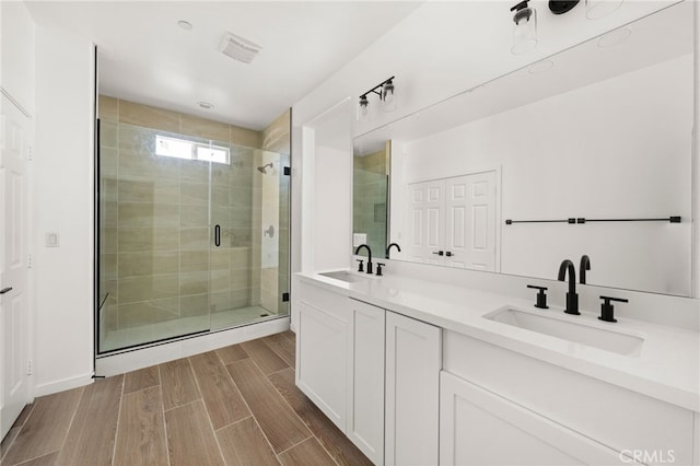 full bath featuring a sink, wood finish floors, double vanity, and a shower stall