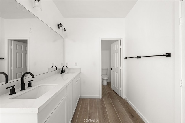 bathroom featuring a sink, toilet, double vanity, and wood tiled floor