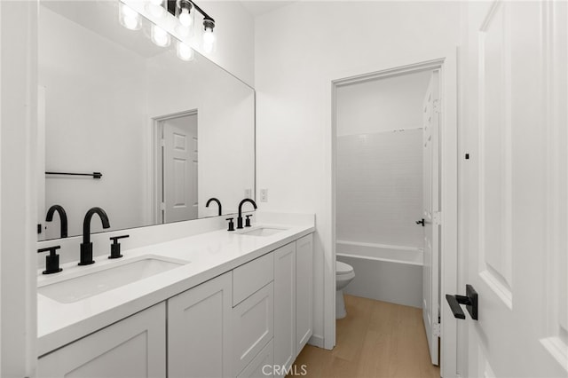 bathroom with double vanity, toilet, wood finished floors, and a sink