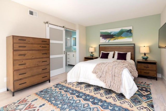 bedroom featuring light wood-type flooring, ensuite bathroom, and a barn door