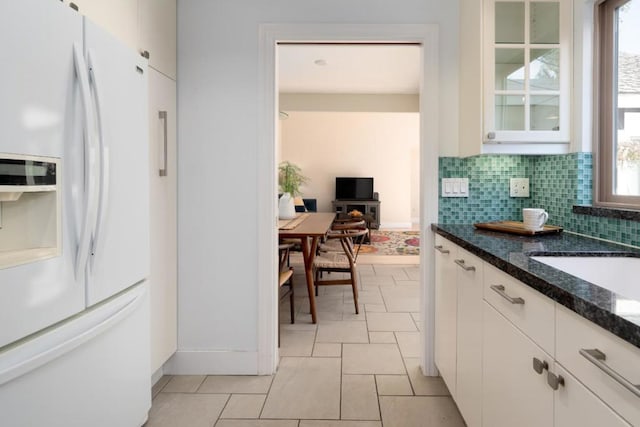 kitchen featuring white cabinets, white fridge with ice dispenser, light tile patterned flooring, and decorative backsplash