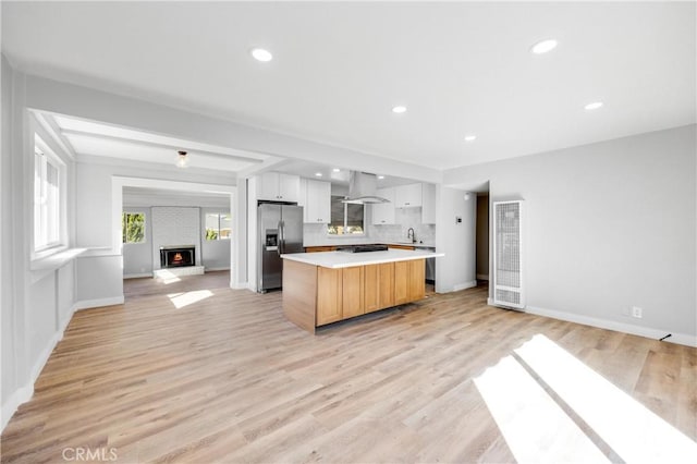 kitchen with a large fireplace, stainless steel fridge, open floor plan, a center island, and island exhaust hood