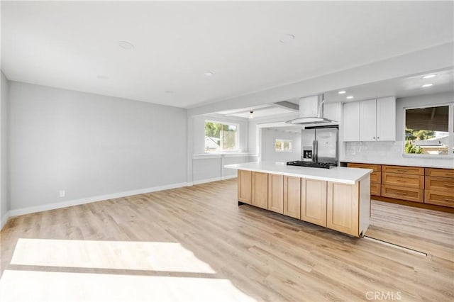 kitchen featuring a kitchen island, wall chimney range hood, decorative backsplash, light wood finished floors, and stainless steel fridge