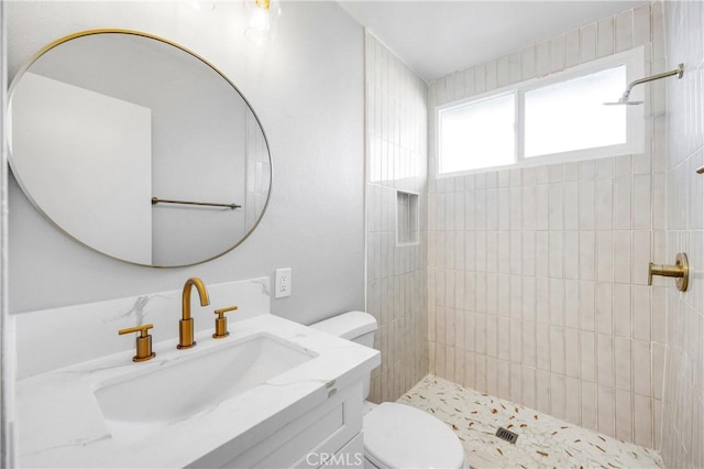 bathroom featuring a tile shower, vanity, and toilet