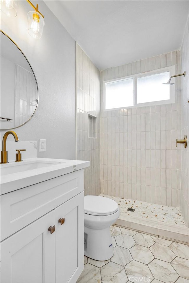 bathroom featuring toilet, marble finish floor, tiled shower, and vanity