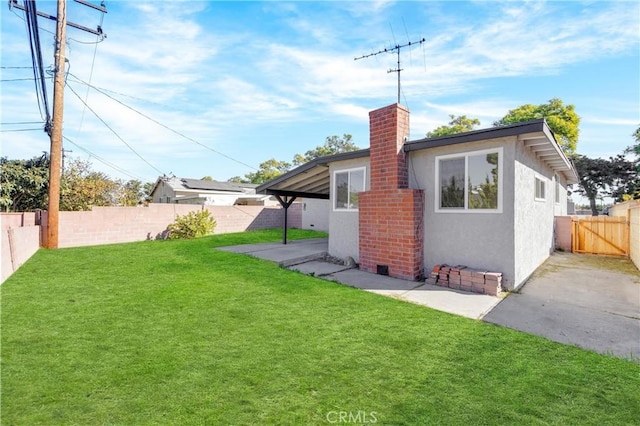 rear view of house featuring a yard, a fenced backyard, a chimney, and stucco siding