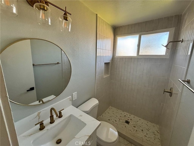 full bathroom featuring toilet, vanity, tiled shower, and a textured wall