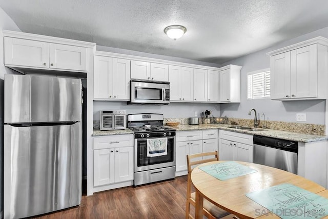 kitchen featuring stainless steel appliances, white cabinetry, sink, and light stone countertops