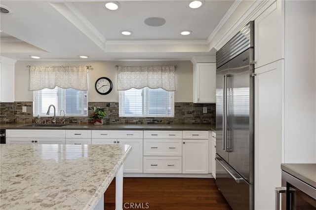 kitchen with a tray ceiling, white cabinetry, stainless steel built in fridge, and sink