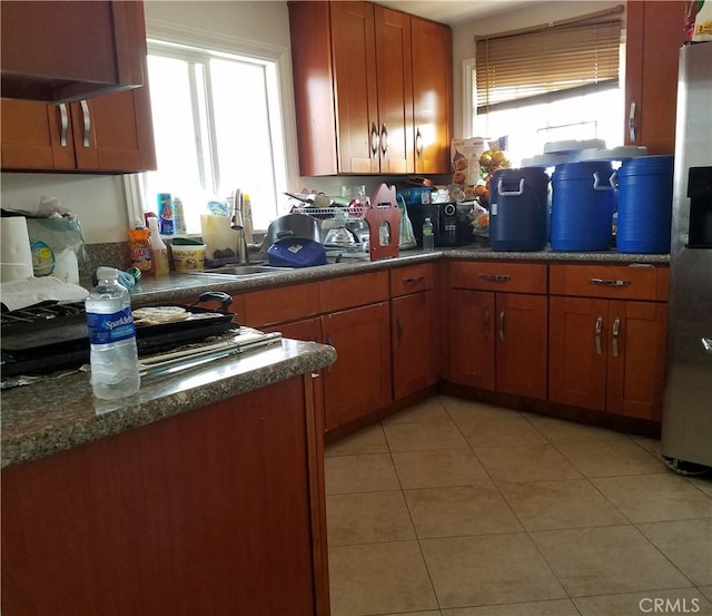 kitchen featuring stainless steel fridge, dark stone countertops, light tile patterned floors, and sink