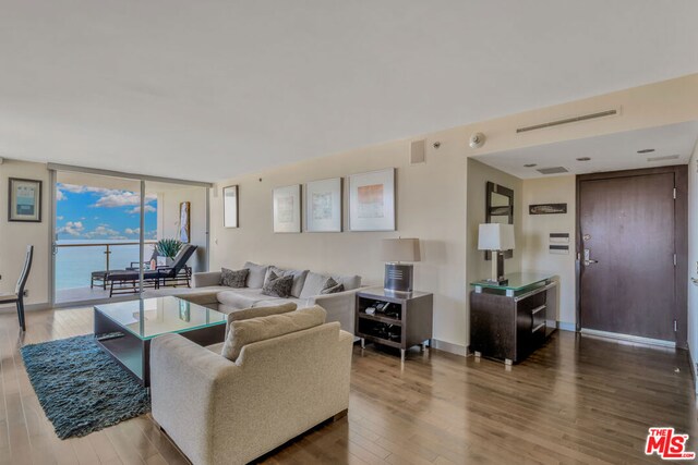 living room with a wall of windows, a water view, and hardwood / wood-style flooring