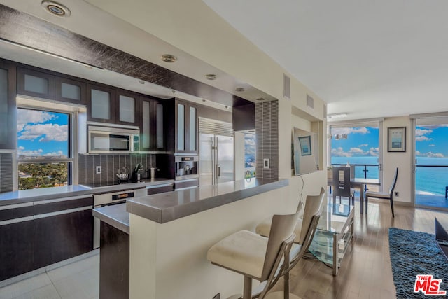 kitchen with appliances with stainless steel finishes, backsplash, dark brown cabinets, a water view, and a center island