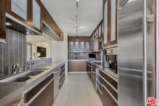 kitchen with track lighting, tasteful backsplash, dark brown cabinetry, sink, and stainless steel refrigerator