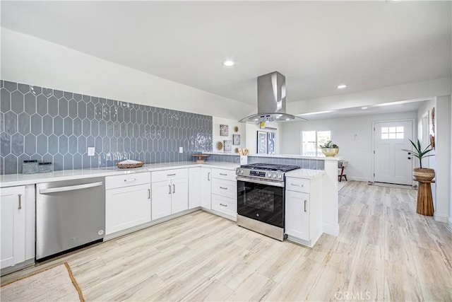 kitchen with stainless steel appliances, light countertops, backsplash, and island range hood