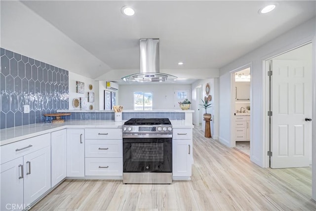 kitchen featuring island exhaust hood, light countertops, light wood-style flooring, white cabinetry, and stainless steel gas range