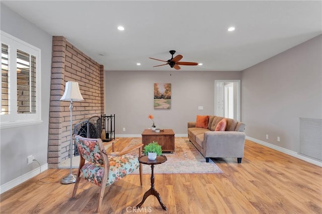 living room featuring ceiling fan, a fireplace, and light wood-type flooring